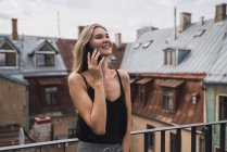 Sorridente donna bionda al telefono in piedi sul balcone e guardando in alto — Foto stock