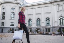 Модная молодая женщина с сумкой для покупок ходит по улице — стоковое фото