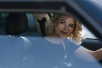 Mujer sonriente en el coche mirando hacia los lados - foto de stock