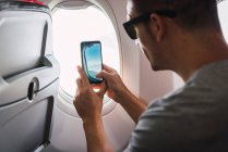 Uomo in aereo, utilizzando smartphone, scattando una foto, finestra dell'aereo — Foto stock