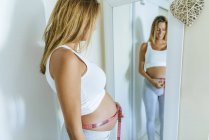Donna incinta che misura la pancia davanti allo specchio — Foto stock