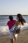 Mãe e filha em pé na praia ao pôr do sol — Fotografia de Stock