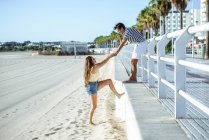 Homem ajudando mulher a subir da praia para o passeio — Fotografia de Stock