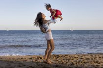 Mother and daughter having fun on the beach, pretending to fly — Stock Photo