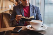 Uomo d'affari seduto nel ristorante a bere caffè e controllare il suo taccuino — Foto stock