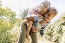 Glückliche Mutter trägt Tochter huckepack in Garten — Stockfoto