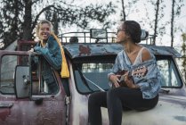 Dois amigos sentados em um caminhão quebrado, jogando o ukulele — Fotografia de Stock