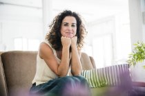 Donna sicura seduta sul suo divano, sorridente — Foto stock