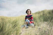 Літня жінка розслабляє на пляжі, сидячи в дюнах — стокове фото