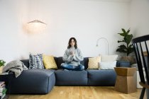 Donna seduta a gambe incrociate sul divano con gli occhi chiusi, meditando a casa — Foto stock