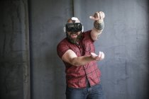 Uomo barbuto che indossa occhiali VR al muro grigio e gioca, gesticolando con le mani — Foto stock