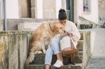Молодая женщина со своей золотистой собакой-ретривером на лестнице смотрит в рюкзак — стоковое фото