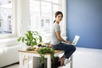 Woman sitting on kitchen table, searching for healthy recipes, using laptop — Stock Photo