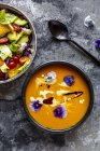 Ciotola di insalata mista con fiori commestibili e ciotola di zuppa di zucca cremata guarnita con fiori commestibili — Foto stock