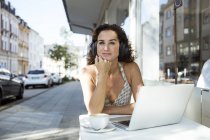 Mature woman sitting in cafe, wearing headphones, using laptop — Stock Photo