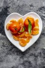 Tangerines avec feuilles, morceaux sur plaque en forme de cœur — Photo de stock