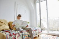 Young man sitting on couch at home and reading map — Stock Photo