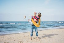 Happy man carrying his wife on his arms on the beach — Stock Photo
