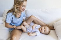 Happy mother playing with her baby girl on couch — Stock Photo