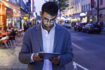 Deutschland, münchen, junger unternehmer in der dämmerung mit digitalem tablet in der stadt — Stockfoto