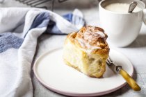 Home-baked cinnamon bun with icing sugar and a cup of coffee — Stock Photo
