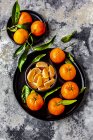Mandarinas con hojas, en plato y trozos en tazón - foto de stock