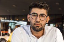 Portrait of pensive young businessman with beard and glasses at sidewalk cafe — Stock Photo