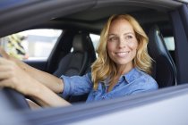 Smiling woman driving car and looking out of window — Stock Photo