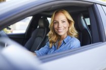 Retrato de mujer sonriente conduciendo coche y mirando por la ventana - foto de stock