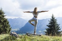 Germania, Baviera, Oberammergau, giovane donna che fa yoga sulla panchina sul prato di montagna — Foto stock