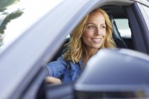 Sorrindo mulher dirigindo carro olhando pela janela — Fotografia de Stock