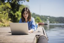 Mujer madura trabajando en un lago, usando un portátil en un embarcadero - foto de stock