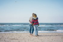 Couple de ture debout sur la plage avec les bras autour, en regardant la mer — Photo de stock