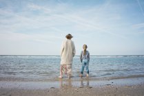 Mãe e filha em pé na praia, olhando para o mar, vista traseira — Fotografia de Stock