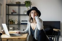 Mature woman with hat, sitting at home, using laptop — Stock Photo