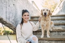 Портрет улыбающейся молодой женщины со своей золотистой собакой-ретривером на лестнице — стоковое фото