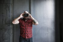 Homme barbu portant et ajustant des lunettes VR au mur gris — Photo de stock