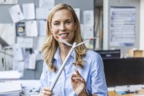 Portrait of smiling woman in office holding wind turbine model — Stock Photo
