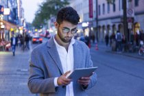 Deutschland, münchen, junger unternehmer in der dämmerung mit digitalem tablet in der stadt — Stockfoto