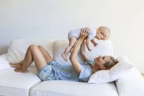 Щаслива мати лежав на дивані і тримає її дитину дівчина — стокове фото