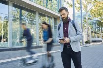 Businessman using cell phone with commuters riding on scooters — Stock Photo