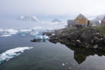 Greenland, Sermersooq, Kulusuk, wooden huts at the shore and ice floating on water — Stock Photo