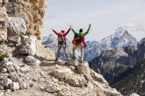 Italy, Cortina d'Ampezzo, couple with rope and climbing equipment looking at view with raised arms — Stock Photo