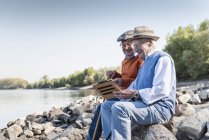 Zwei alte Freunde sitzen am Flussufer und benutzen ein digitales Tablet — Stockfoto