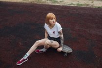 Coole junge Frau sitzt auf Carver-Skateboard im Freien — Stockfoto