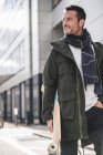 Reifer Mann, trägt Mantel und Schal, spaziert durch die Stadt, trägt Longboard — Stockfoto