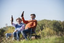 Dos viejos amigos sentados en el campo, bebiendo cerveza, hablando de los viejos tiempos - foto de stock