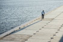 Junger Mann mit Fahrrad auf Uferpromenade am Ufer — Stockfoto