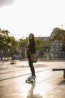 Young woman with cell phone riding longboard in the city — Stock Photo