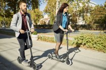 Businessman and businesswoman riding scooters — Stock Photo